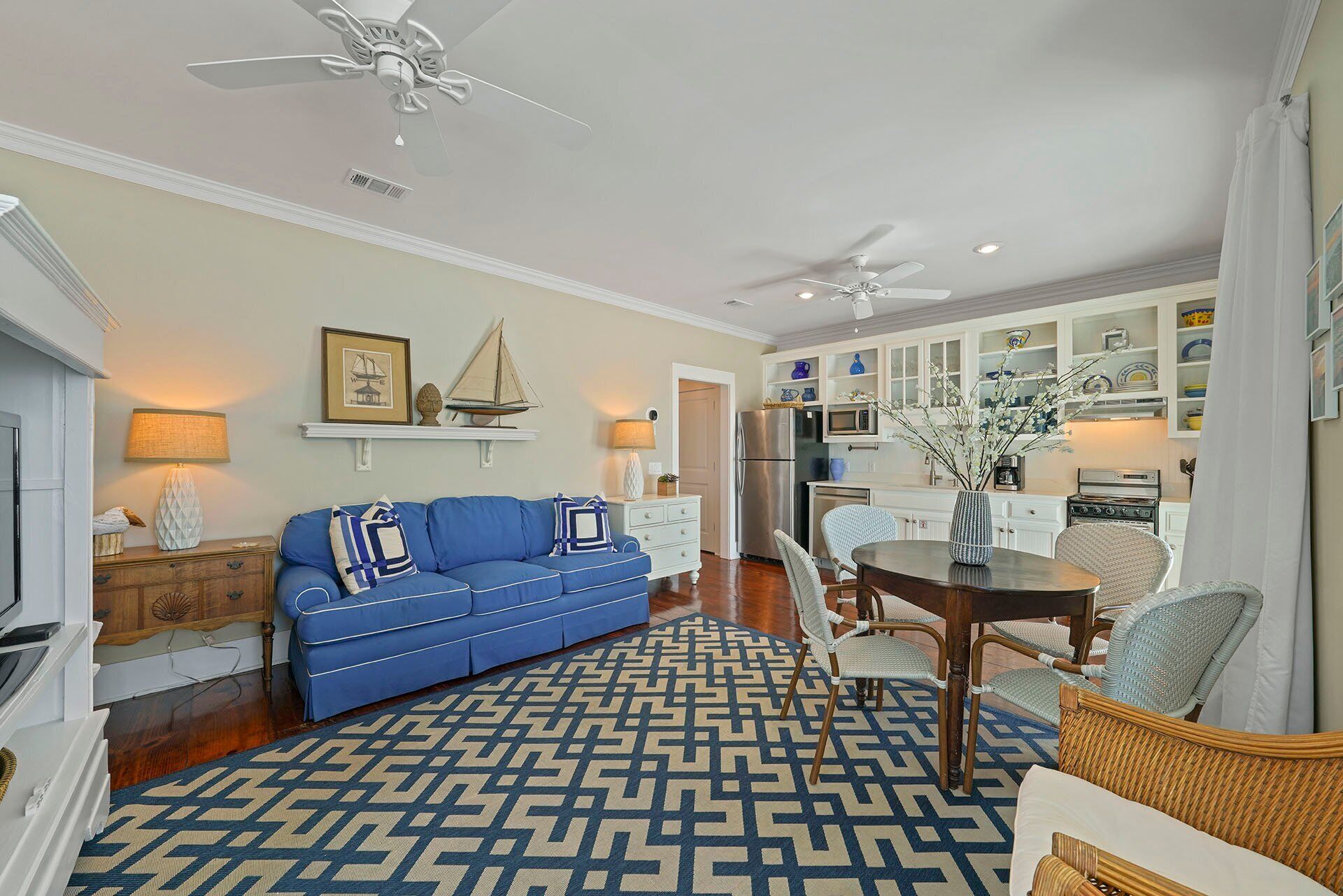 A spacious living room with a blue sofa, a patterned rug, and a dining area with wicker chairs.
