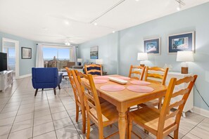 A dining area with a wooden table and chairs, a blue armchair, and a view of the sea through large windows.
