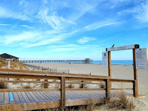 A wooden boardwalk leading to a beach with a pier in the background.