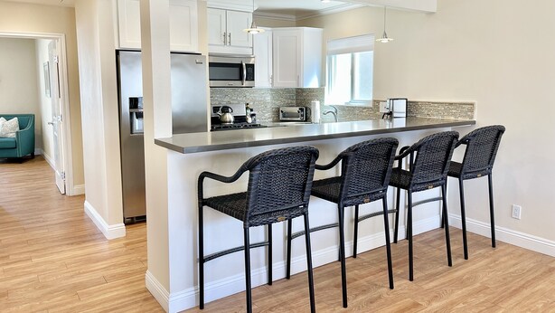 Una cocina moderna con una isla central, taburetes de bar, electrodomésticos de acero inoxidable y vistas al salón.