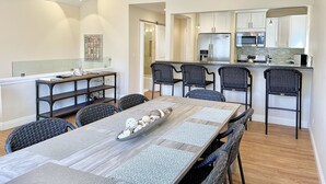 Una cocina moderna con armarios blancos, electrodomésticos de acero inoxidable y una zona de bar con sillas de mimbre.