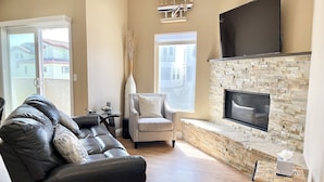Una sala de estar con un sofá de cuero, una chimenea de piedra, un televisor de pantalla plana y un ventanal grande.