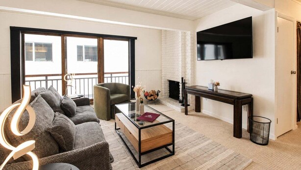 A living room with a sofa, armchair, coffee table, fireplace, TV, and a balcony. - Central Aspen Condo - Prime Price and Location (Aspen)