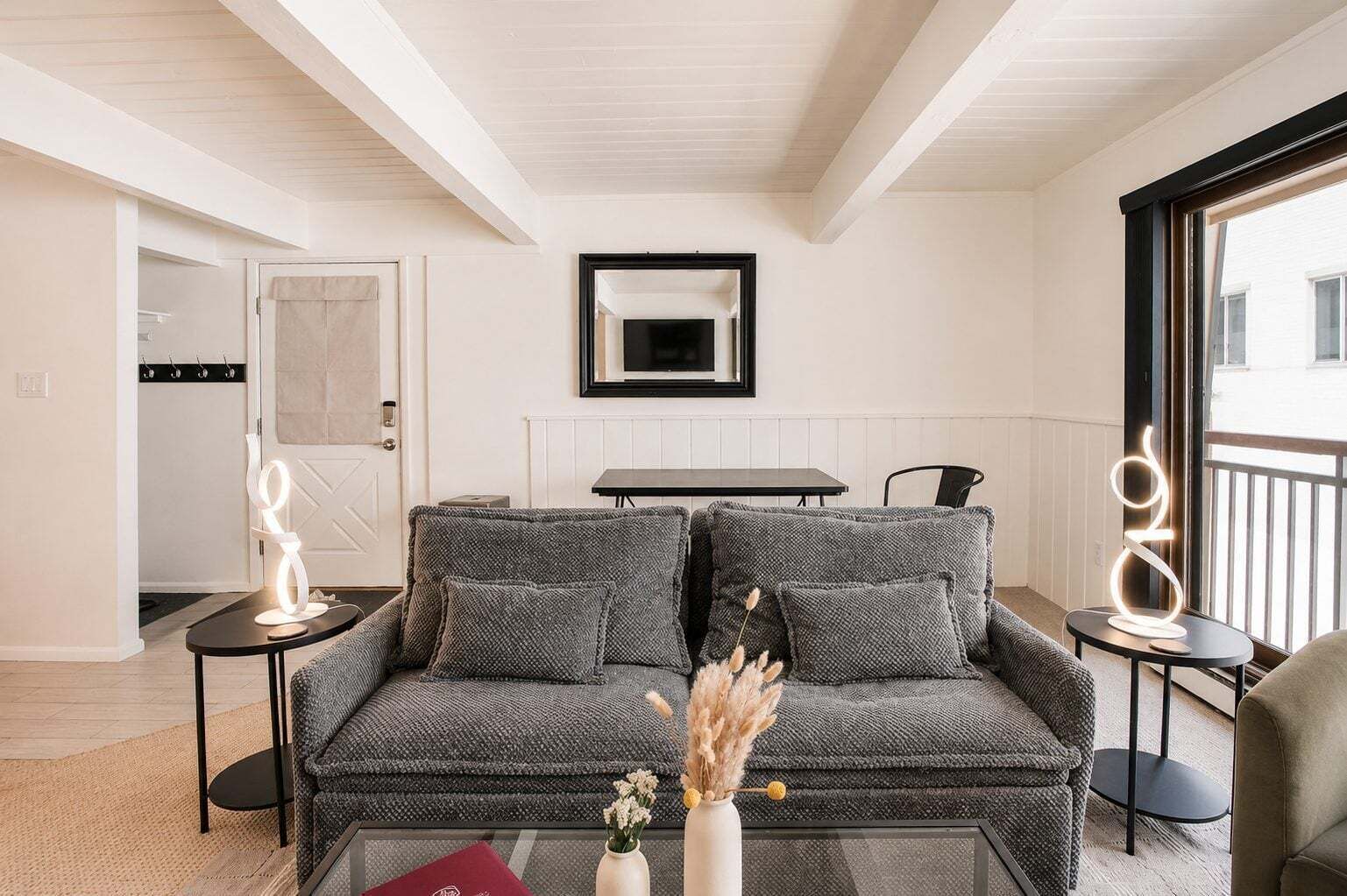 A modern living room with a grey sofa, a glass coffee table, and a vase with dried flowers.
