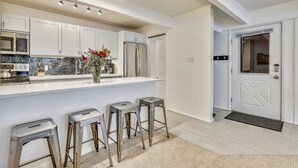 A modern kitchen with white cabinets, stainless steel appliances, and a marble backsplash. There are three bar stools and a vase with flowers on the island. - Central Aspen Condo - Prime Price and Location (Aspen)