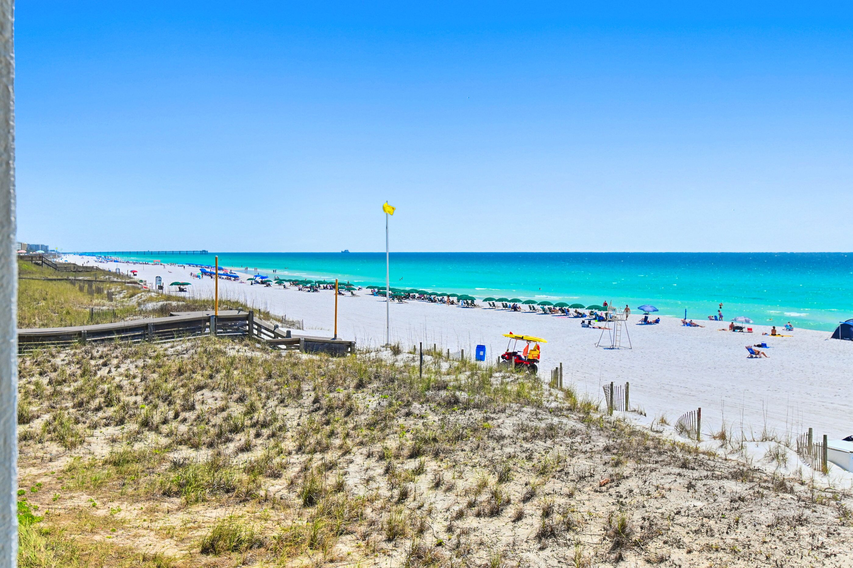 A beach with a wooden boardwalk, a lifeguard tower, and a clear blue sky.