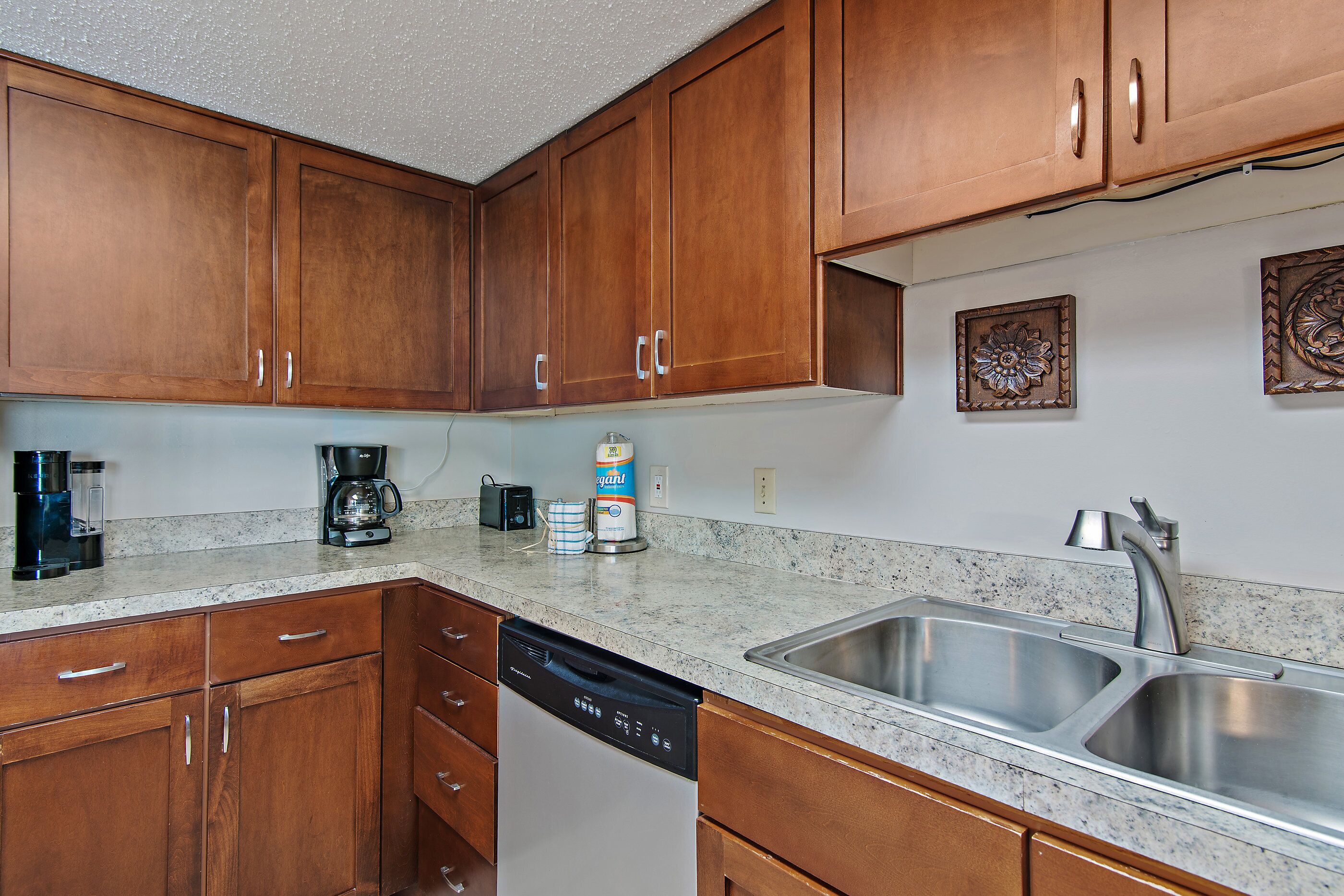 A kitchen with wooden cabinets, a dishwasher, a coffee maker, and a sink.