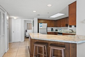 Una cocina con armarios de madera, encimera de mármol y dos taburetes.