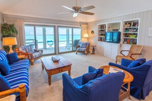 A living room with a view of the ocean, furnished with blue sofas, a coffee table, and a bookshelf.
