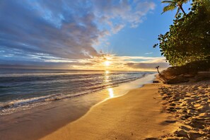 A beach with a clear sky, calm sea, and a sunset.