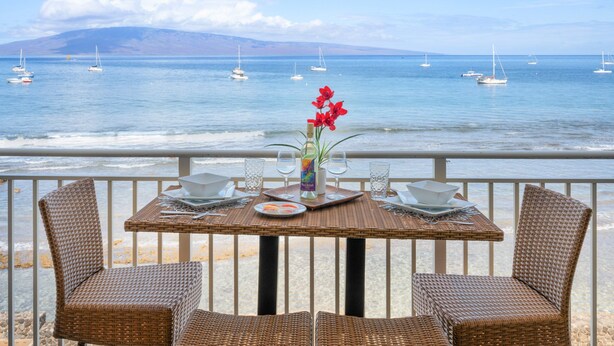 Una mesa de comedor con sillas de mimbre y vistas al mar con barcos.