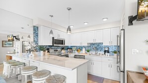 Una cocina moderna con armarios blancos, una isla grande con taburetes de bar, un microondas y un refrigerador.
