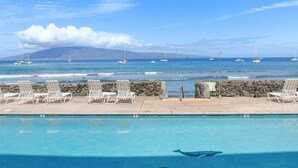 Zona junto a la piscina con sillones de descanso y vistas al océano y veleros.