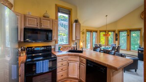 A kitchen with wooden cabinets, a black stove, and a dishwasher. There is a large window with a view of trees. - Pet Friendly 2-bedroom, 2-bathroom condo, Manitou #101 and those views! (Telluride)