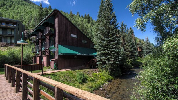A rustic wooden building with a green awning, a wooden deck, and a river in the background. - Pet Friendly 2-bedroom, 2-bathroom condo, Manitou #101 and those views! (Telluride)