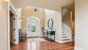 A spacious foyer with a wooden floor, a bench, a desk with drawers, a mirror, and a staircase. - Golf Front, Premium built. Pool, hot tub, gameroom, theater room. Dogs ok. (Corolla)