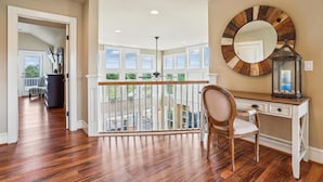 A spacious room with hardwood flooring, a desk with a chair, a large mirror, and a balcony with a railing. - Golf Front, Premium built. Pool, hot tub, gameroom, theater room. Dogs ok. (Corolla)