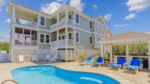 A multi-story building with a pool area, including a pool, lounge chairs, and a covered seating area. - Golf Front, Premium built. Pool, hot tub, gameroom, theater room. Dogs ok. (Corolla)