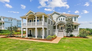 A two-story house with a porch, a covered front entrance, and a landscaped front yard. - Golf Front, Premium built. Pool, hot tub, gameroom, theater room. Dogs ok. (Corolla)