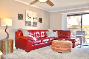 A red leather sofa, a striped ottoman, and a ceiling fan in a living room with artwork on the walls.