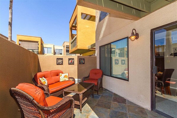 An outdoor patio area with wicker furniture, a glass door leading to a room, and a view of neighboring buildings. - Endless Summer Modern 2 Bedroom Condo/ Community Pool/ Jacuzzi/ Scottsdale (Scottsdale)