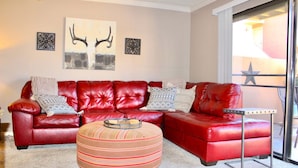 A living room with a red leather sofa, a striped ottoman, and two wall-mounted decorative pieces. - Endless Summer Modern 2 Bedroom Condo/ Community Pool/ Jacuzzi/ Scottsdale (Scottsdale)