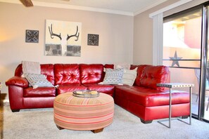 A living room with a red leather sofa, a striped ottoman, and two wall-mounted decorative pieces.