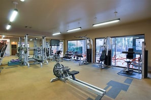 A gym with various exercise equipment, large windows, and a carpeted floor.
