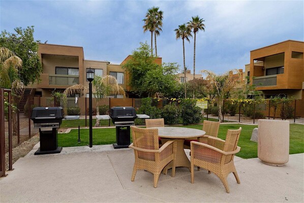 An outdoor patio with wicker furniture, two barbecue grills, and a large planter.