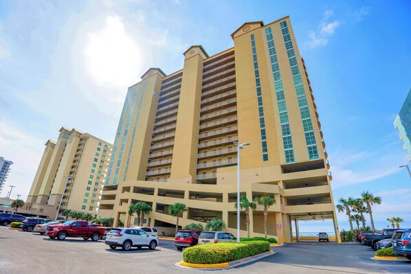 A multi-story hotel with a parking garage, palm trees, and a clear sky.