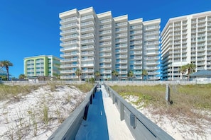 A beachfront hotel with multiple floors, a boardwalk leading to the beach, and palm trees.
