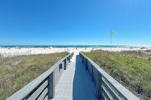 A wooden boardwalk leading to a beach with a flag on a pole.