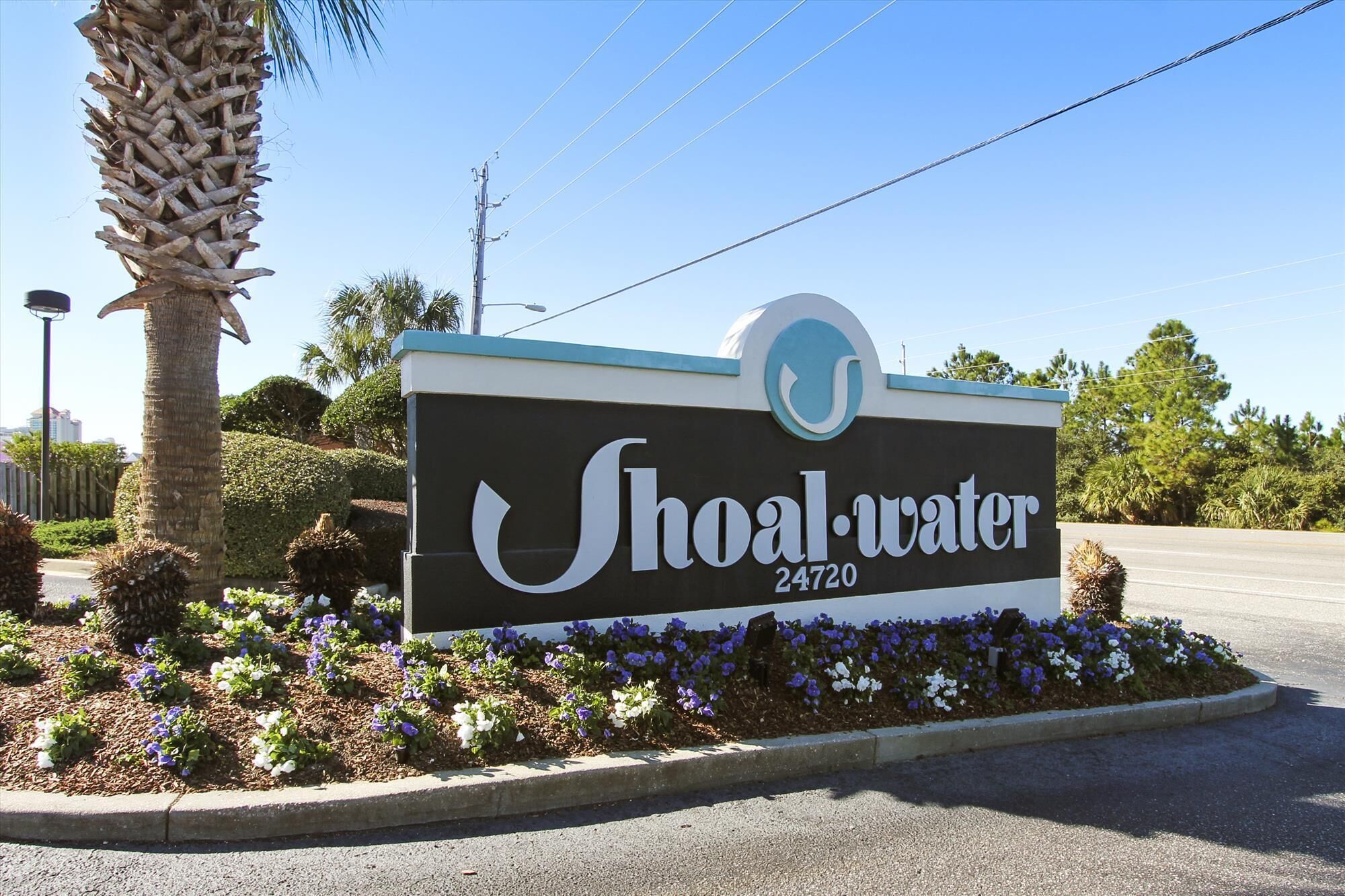 A sign for Shoal-Water with the address 24720, surrounded by a landscaped garden with various plants and flowers.