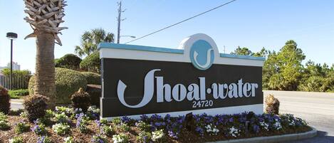 A sign for Shoal-Water with the address 24720, surrounded by a landscaped garden with various plants and flowers.