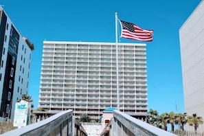 A high-rise hotel with a large American flag on top, featuring a modern architectural design with multiple balconies. - Crystal Tower 407 - Beachfront pool, great amenities & private skywalk to beach! (Gulf Shores)