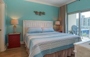 Une chambre à coucher avec un lit, deux tables de chevet avec des lampes, une commode rouge et une vue sur le balcon.