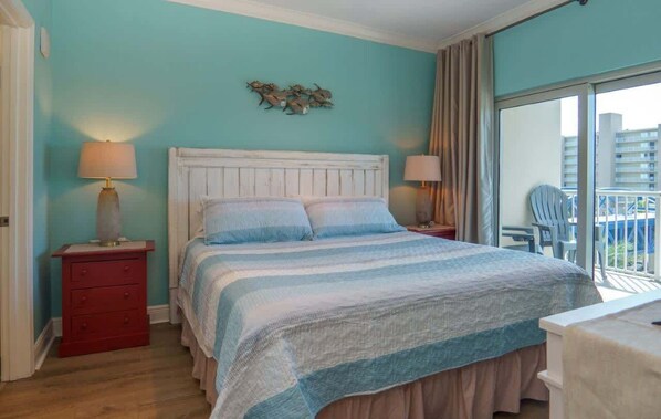 A bedroom with a bed, two bedside tables with lamps, a red dresser, and a view of the balcony.