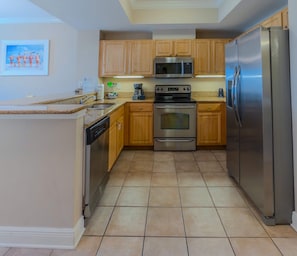 A modern kitchen with wooden cabinets, stainless steel appliances, and a tiled floor. - Crystal Tower 407 - Beachfront pool, great amenities & private skywalk to beach! (Gulf Shores)