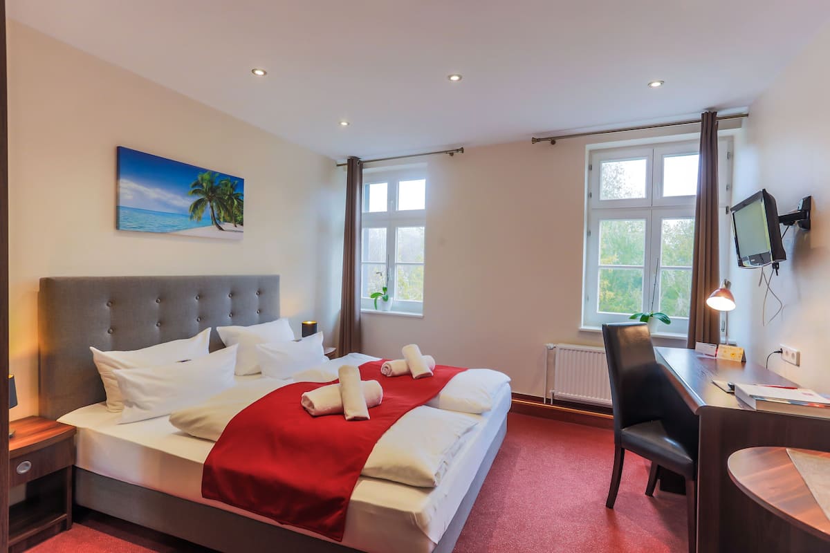 Une chambre d’hôtel avec un lit, un bureau, une chaise, une télévision et une fenêtre avec des rideaux.