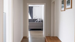 A hallway with a wooden bench, white walls, and a grey sofa in the background. - Hotel Zur Alten Oder Frankfurt (Frankfurt an der Oder)