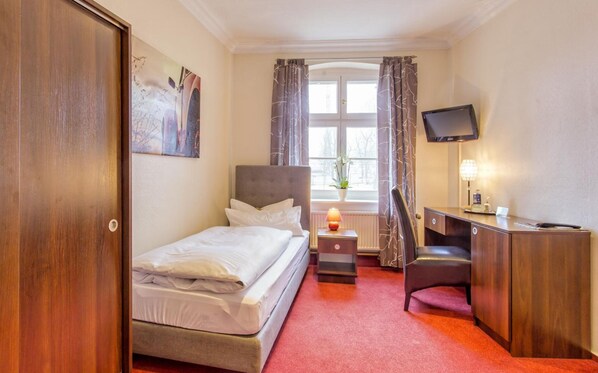 Una habitación de hotel con una cama, un escritorio, una silla, un televisor y una ventana con cortinas.