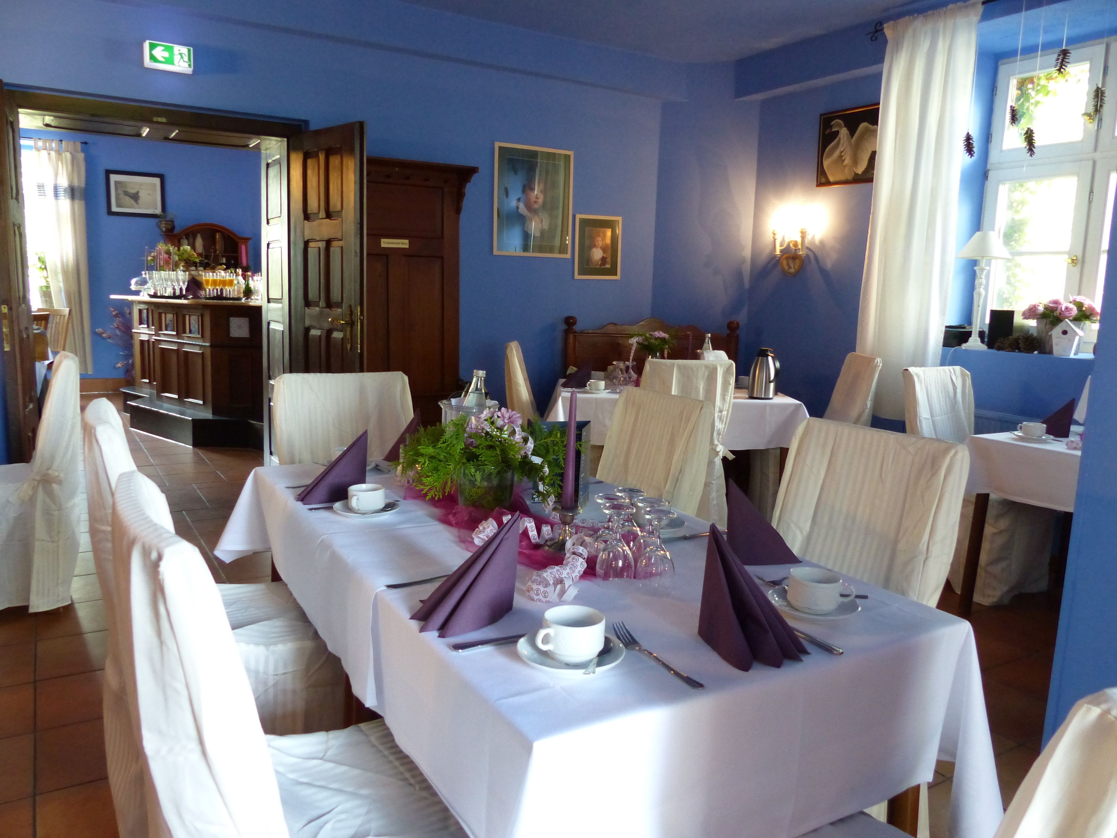 Comedor con una larga mesa dispuesta para una comida, sillas alrededor y una pared azul con cuadros enmarcados.