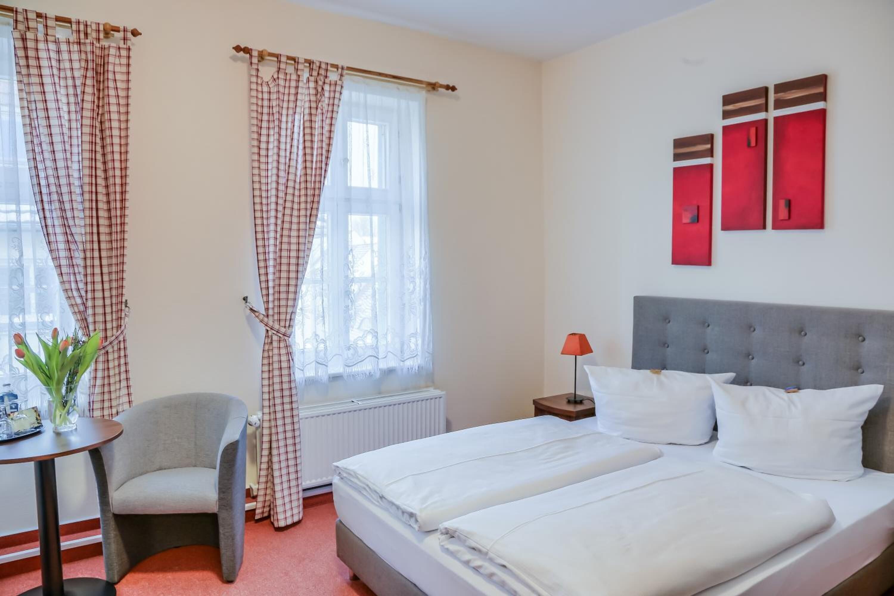 A hotel room with a bed, two bedside tables, a chair, a radiator, and curtains.