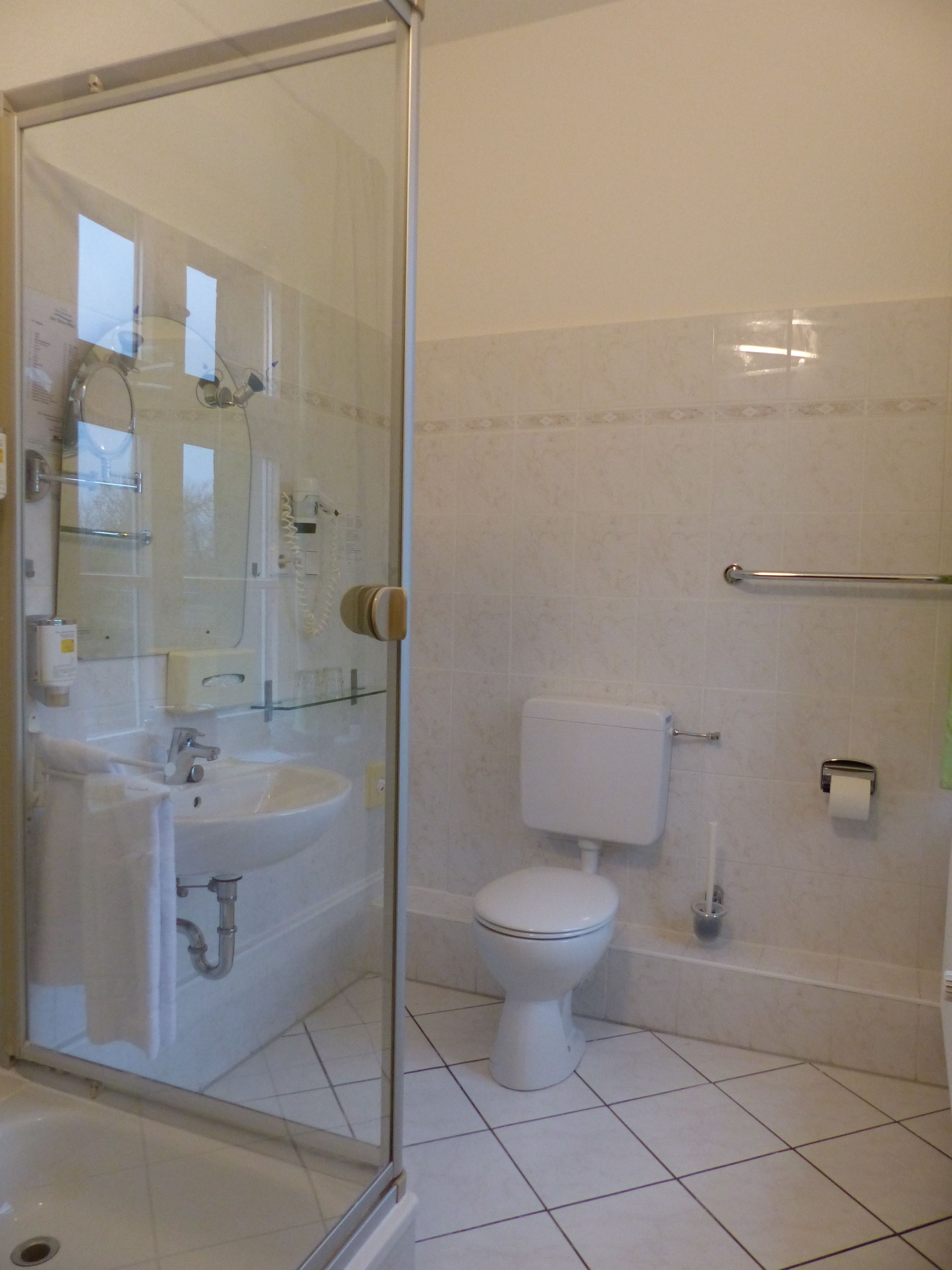 A bathroom with a glass shower enclosure, a sink, a toilet, and a hand dryer.
