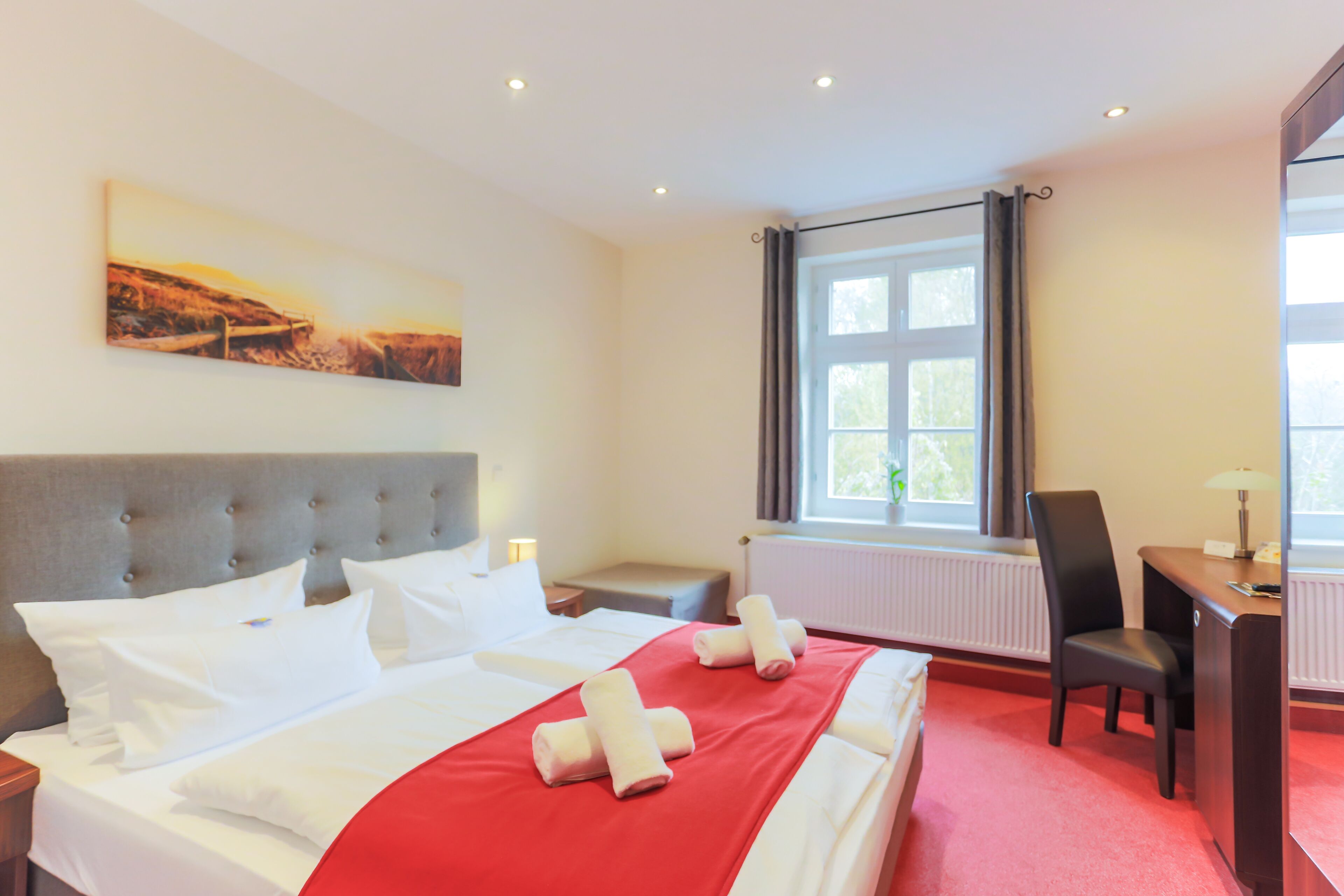 Ein Hotelzimmer mit einem großen Bett, einem Schreibtisch, einem Stuhl, einem Fenster mit Vorhängen und einem Bild an der Wand.