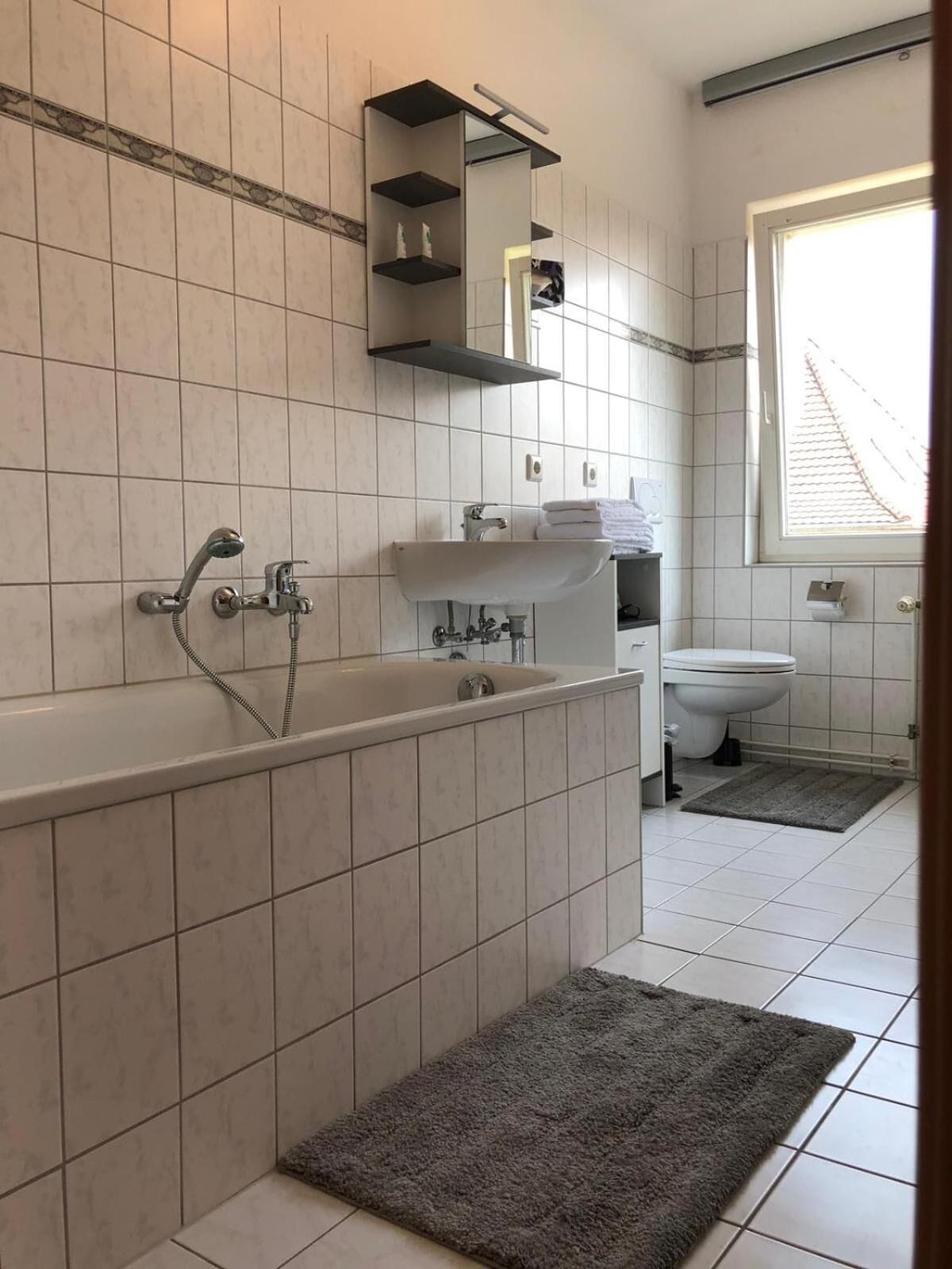 A bathroom with a bathtub, sink, and toilet. There is a window providing natural light and a towel rack above the sink.