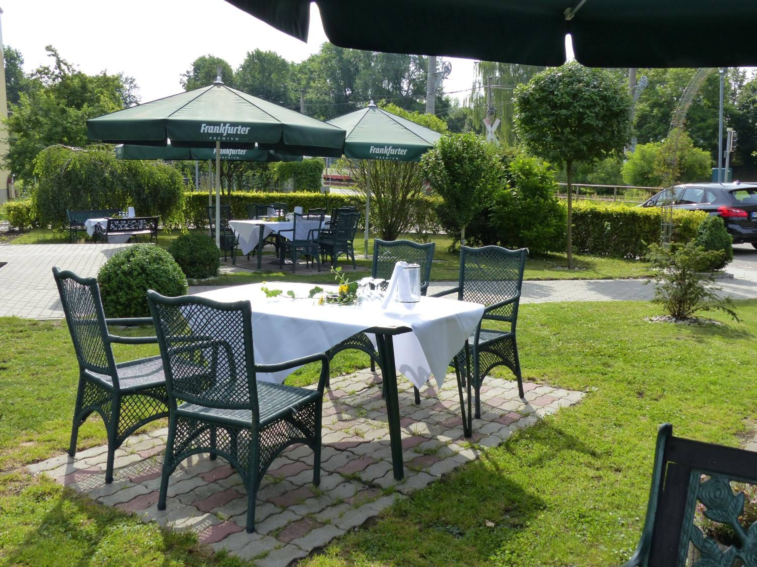 Un área de comedor al aire libre con mesas y sillas, sombrillas verdes y un camino pavimentado.