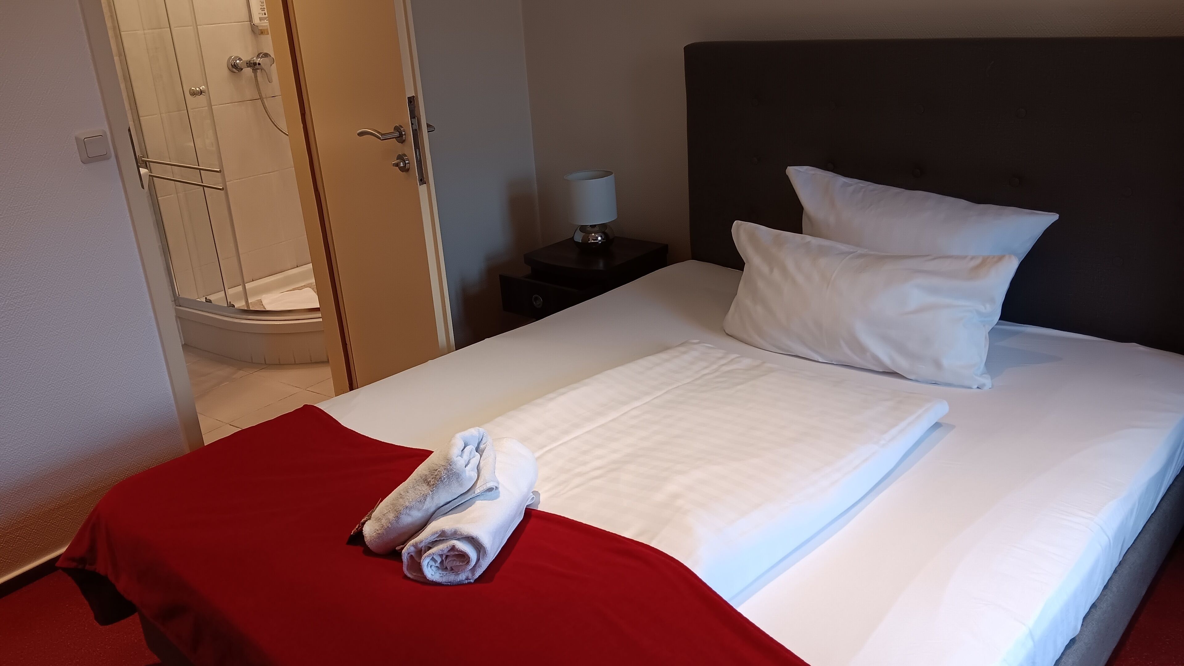 A hotel room with a bed, a red throw blanket, and a towel.