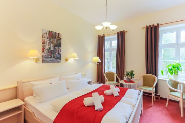 Ein Hotelzimmer mit einem großen Bett, zwei Stühlen, einem kleinen Tisch mit einer Pflanze und einem Bild an der Wand.