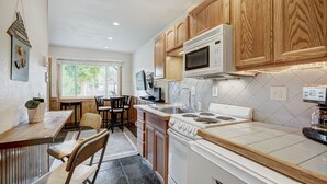 A kitchen with wooden cabinets, a microwave, a stove, and a dining area with chairs and a table. - A Cozy Mtn Abode in the Heart of Breck - Stylish Updates Throughout! | PM3C (Breckenridge)